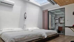 A modern bedroom with a skylight, a bed with white linens, a glass shower enclosure, and a wooden floor.