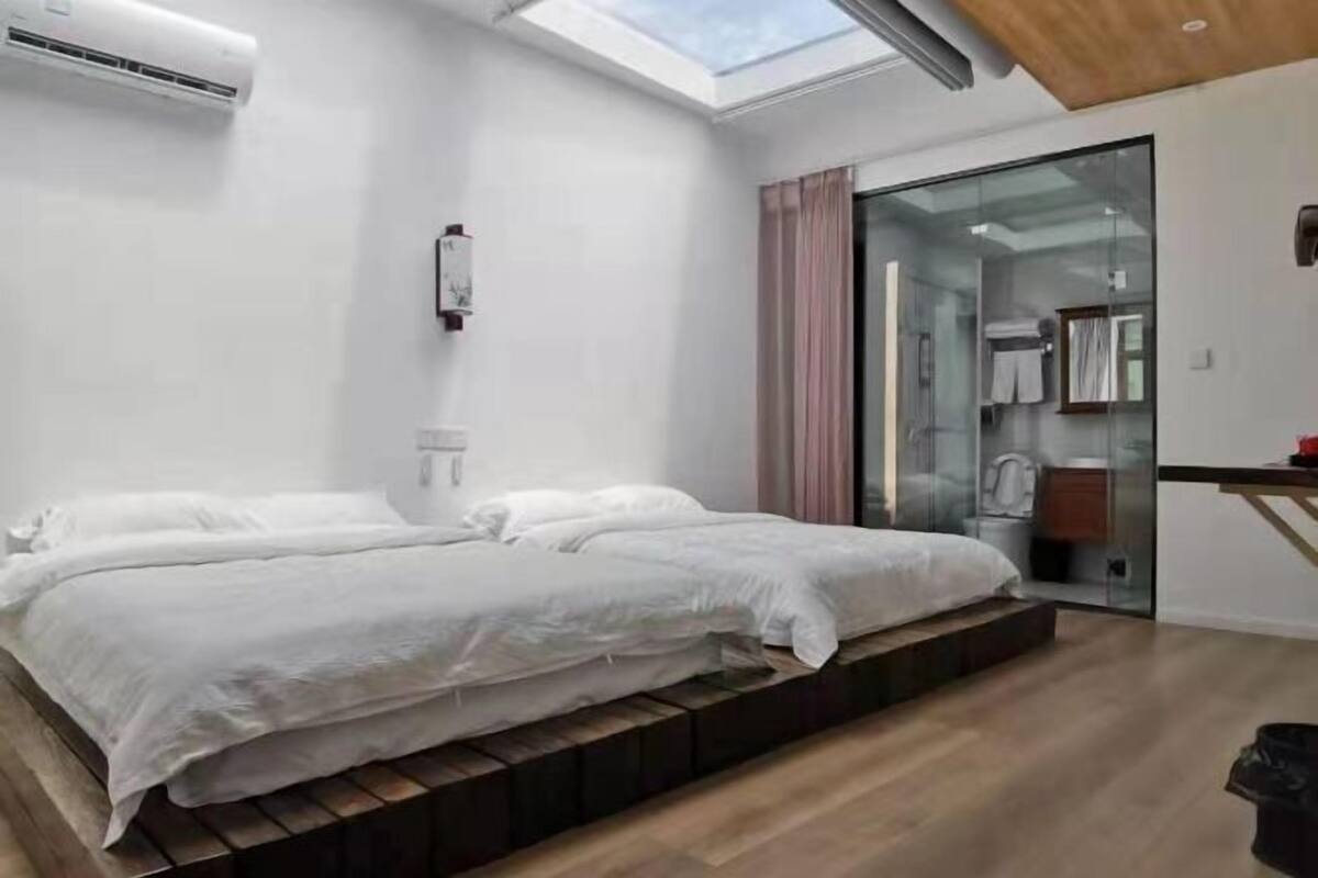 Une chambre moderne avec une lucarne, un lit recouvert de linge de maison blanc, une douche en verre et un plancher en bois.