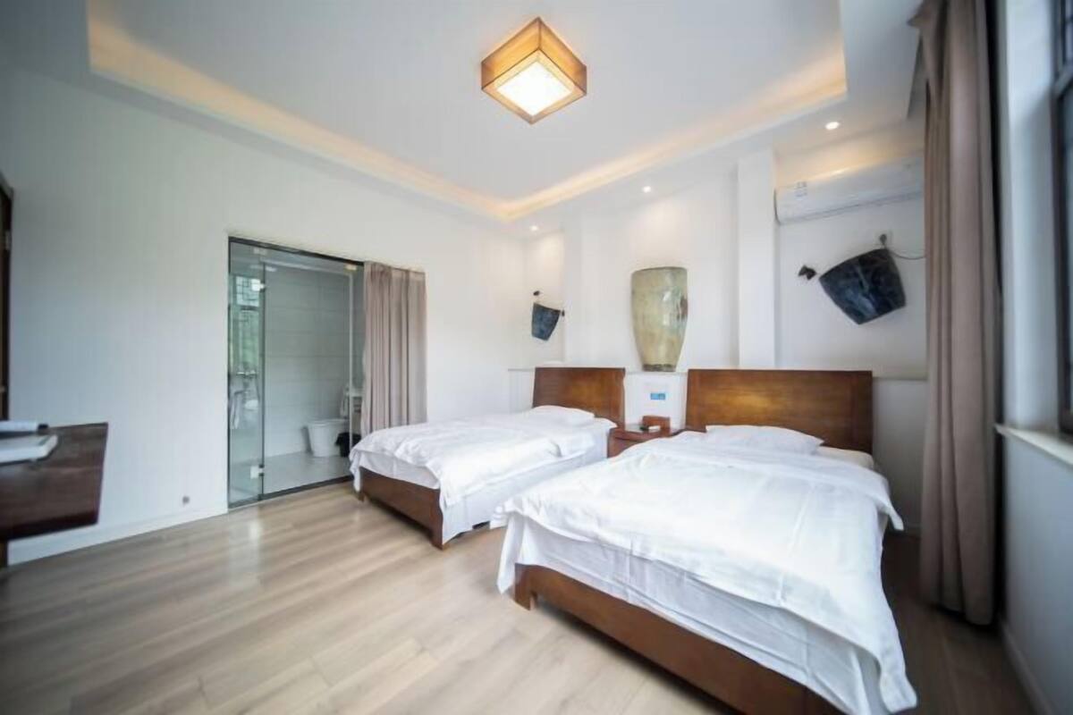 Une chambre d’hôtel avec deux lits, un plancher en bois, un grand vase et un luminaire au plafond.