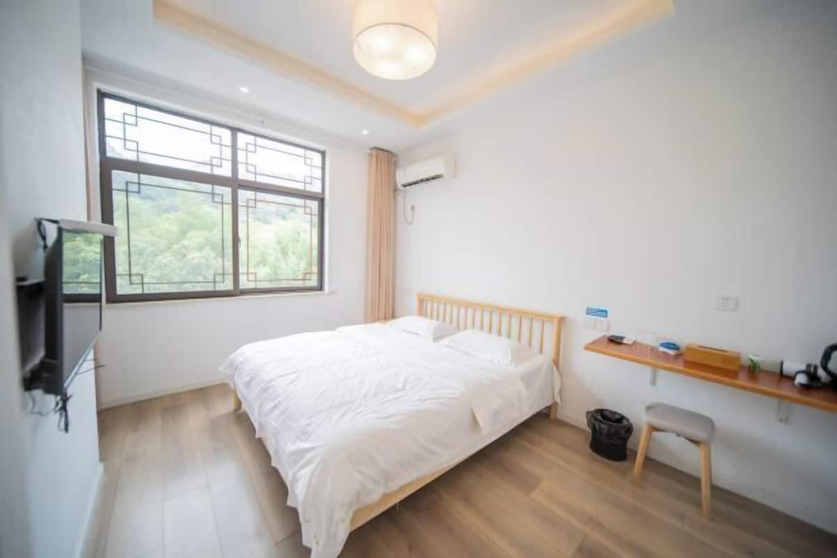 Une chambre à coucher comprenant un lit, une télévision, un bureau, une chaise et une fenêtre donnant sur un paysage verdoyant.