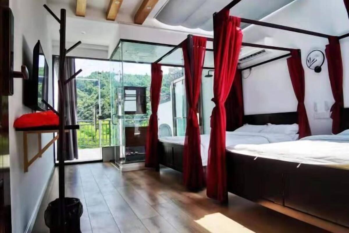 Une chambre à coucher avec un lit, un rideau rouge, une porte vitrée donnant sur un balcon et un plafond en bois.