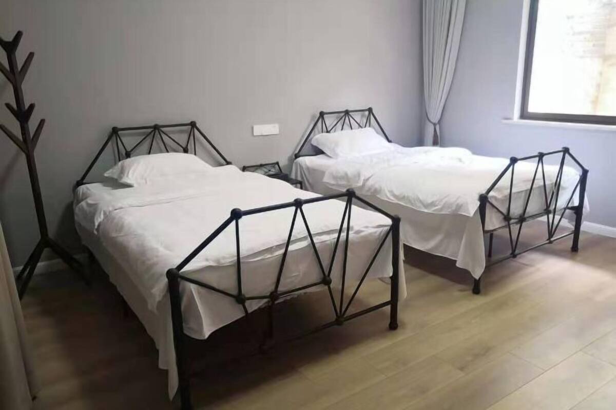 Deux lits jumeaux avec des cadres en métal, un plancher en bois et une fenêtre avec des rideaux.