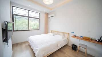 Un dormitorio con cama, televisión, escritorio y ventana con vistas a zonas verdes.
