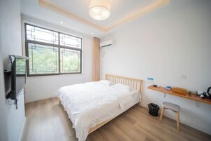Un dormitorio con cama, televisión, escritorio y ventana con vistas a zonas verdes.
