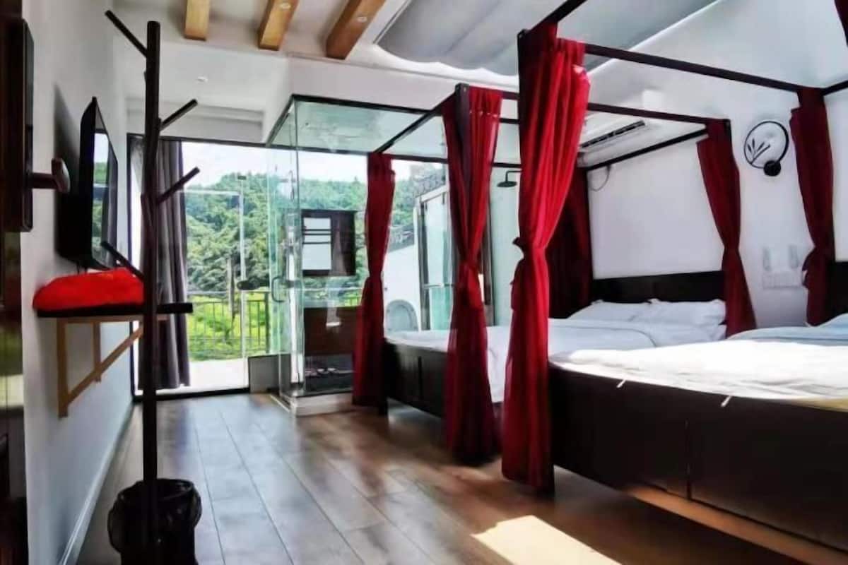 Relax in a serene space with a large bed under a canopy, surrounded by lush views from the glass door leading to a balcony.