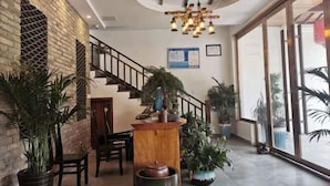 A lobby with a staircase, wooden reception desk, potted plants, and large windows.