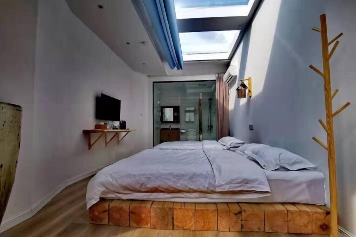 Une chambre avec un puits de lumière, un lit, un téléviseur fixé au mur et un plancher en bois.