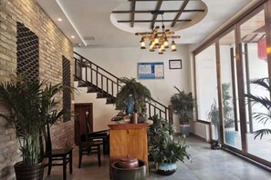 Un hall d’hôtel avec un escalier, un comptoir d’accueil en bois, des plantes en pot et de grandes fenêtres.