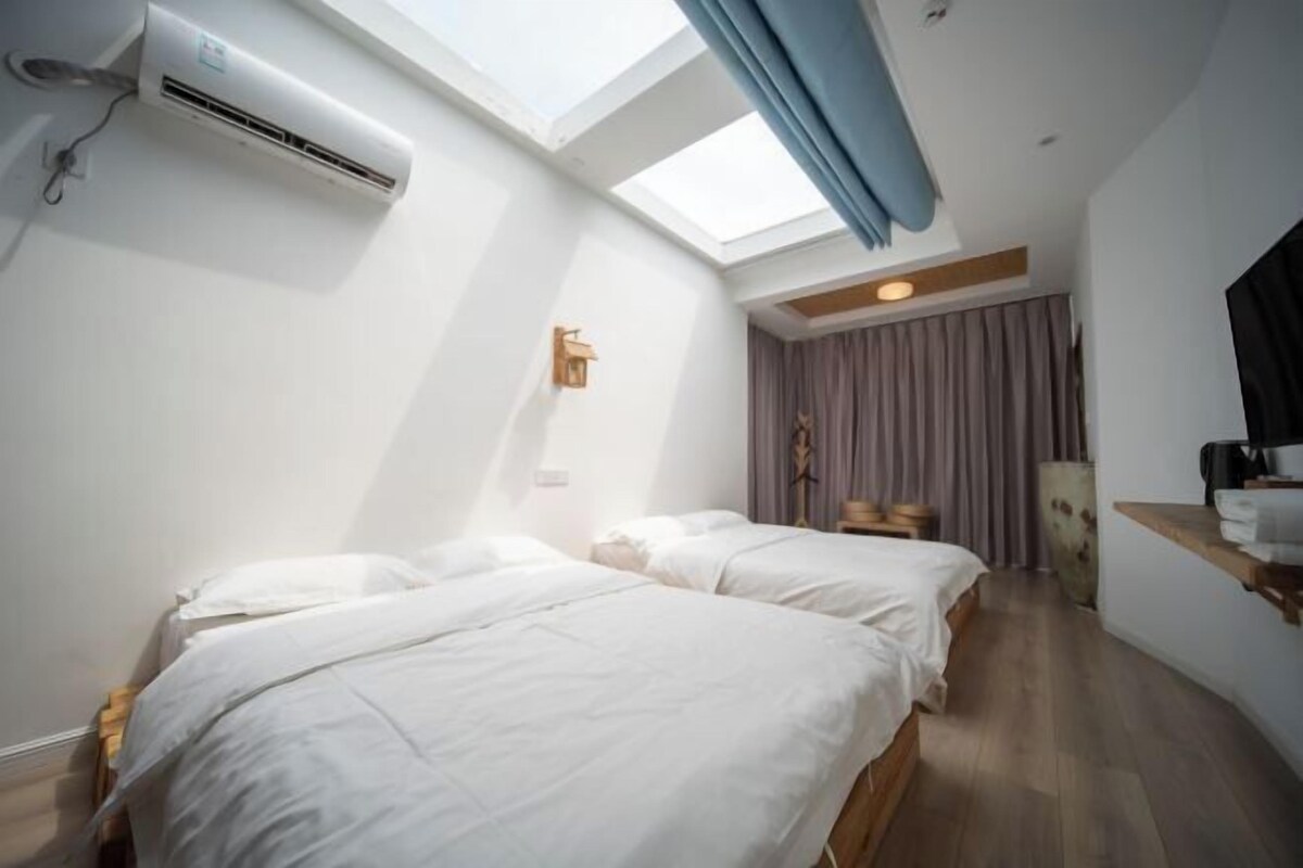 A room with two beds, a skylight, an air conditioning unit, and a wooden floor.