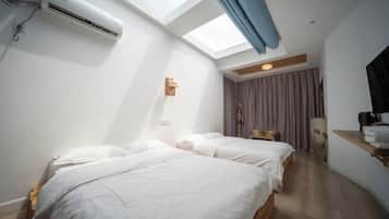 Una habitación con dos camas, un tragaluz, un equipo de aire acondicionado y piso de madera.