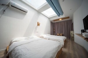 Una habitación con dos camas, un tragaluz, un equipo de aire acondicionado y piso de madera.