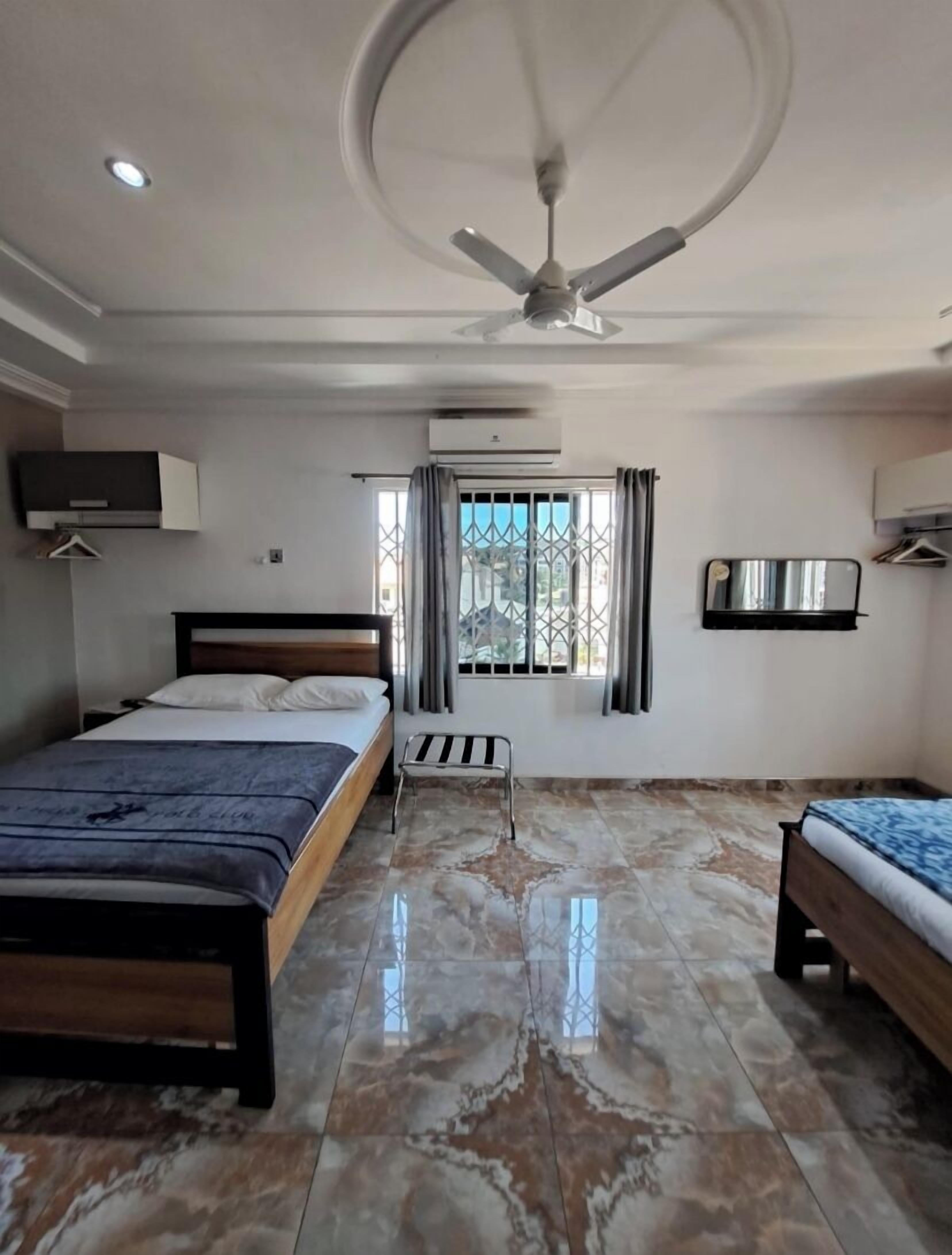 Een slaapkamer met twee bedden, een plafondventilator, een airconditioning en een raam met tralies.