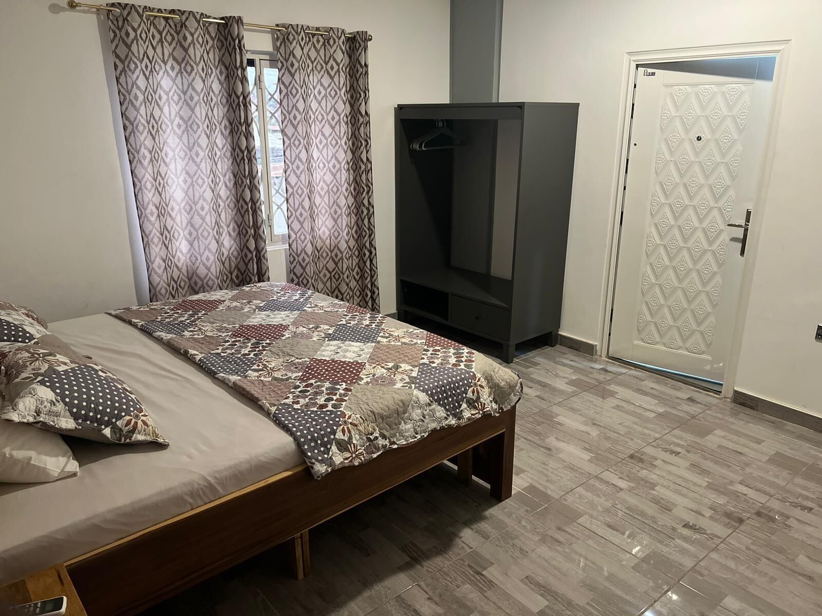 A bedroom with a bed, curtains, a wardrobe, and a door.