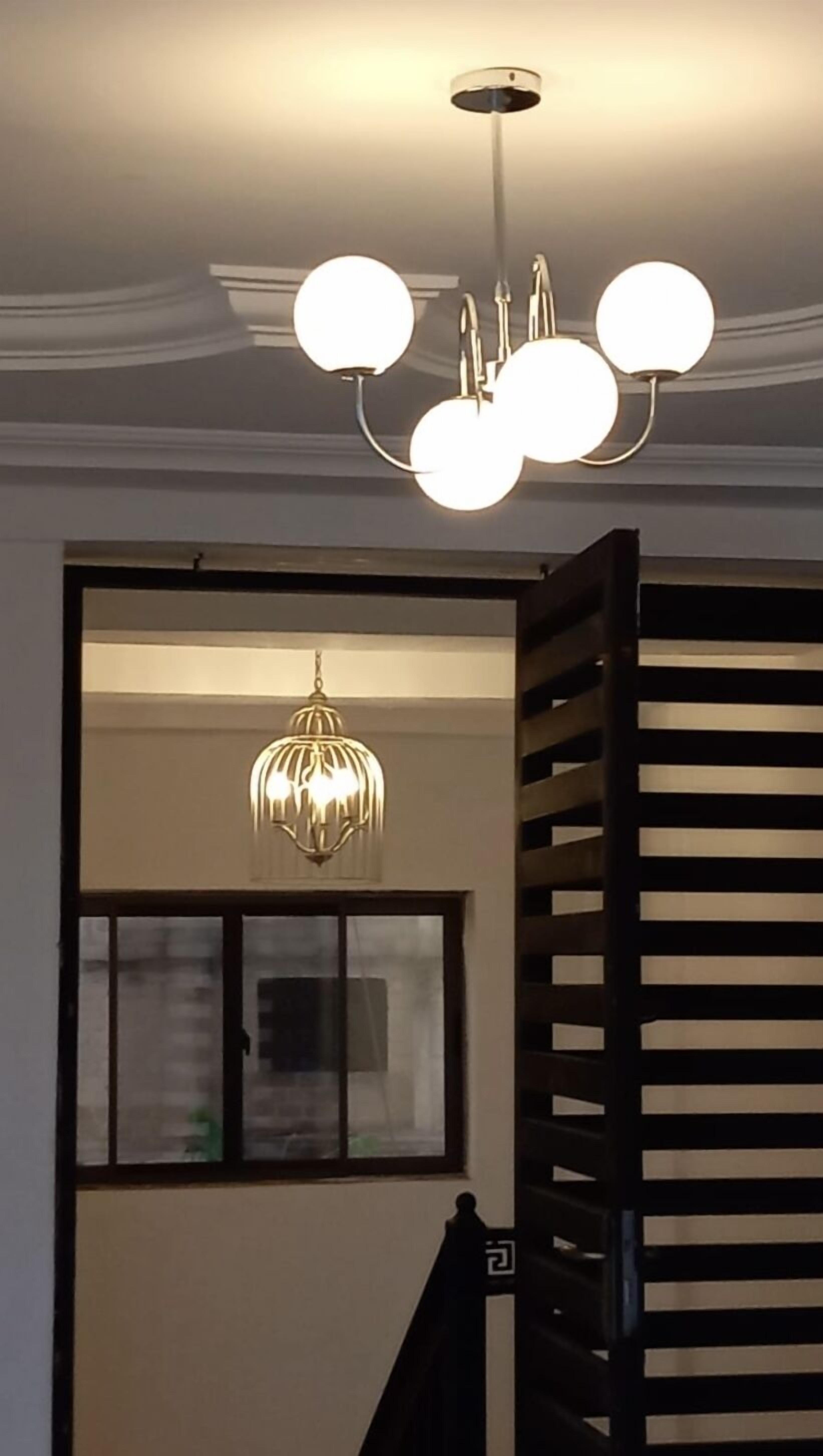 Un escalier avec une rampe noire et un lustre moderne doté de plusieurs lampes sphériques.