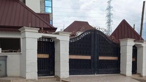 A gated entrance with a metal gate and steps leading up to a building with a red roof and white pillars. - BAFFOUR APARTMENTS (Kumasi)