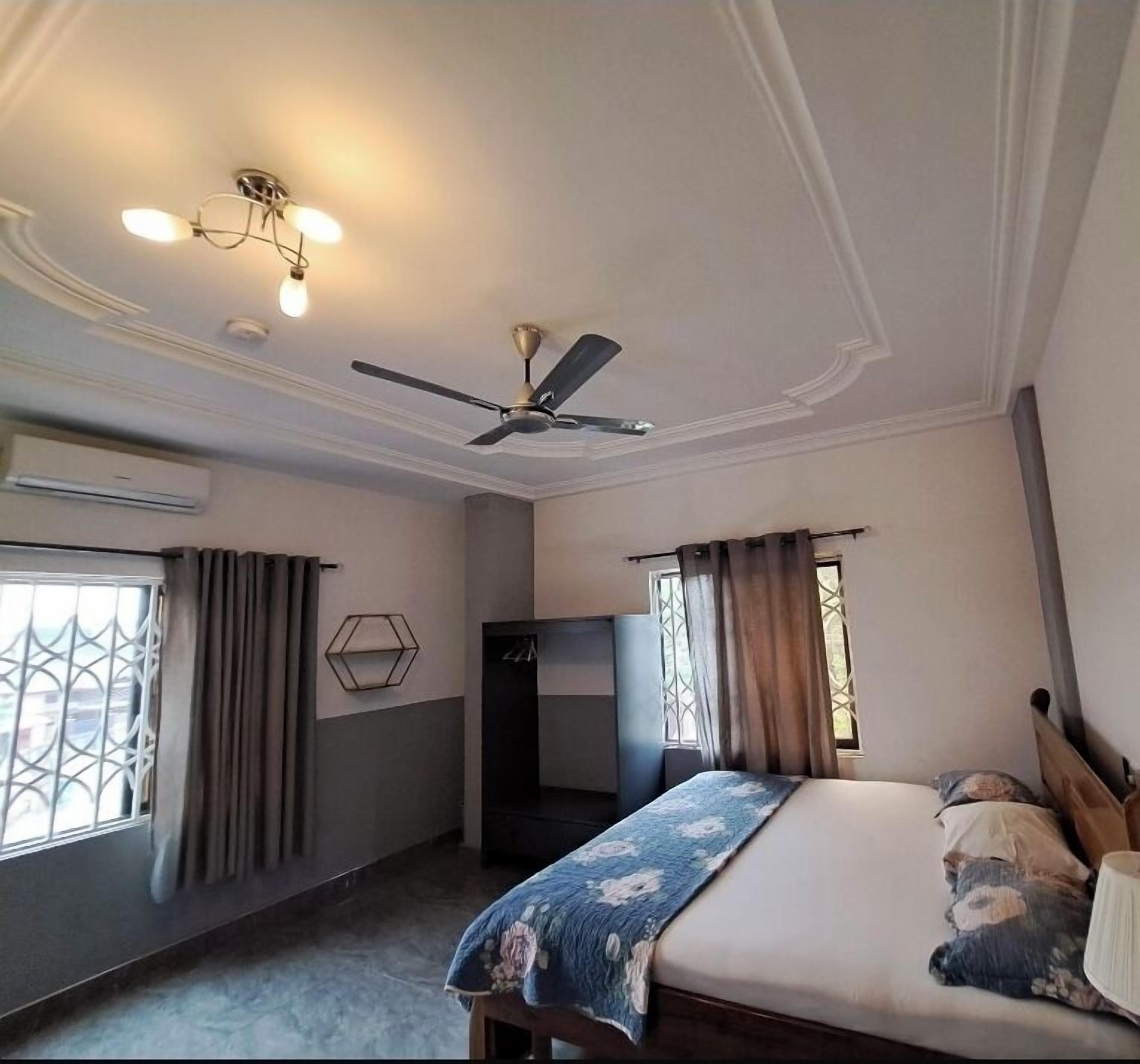 Ein Schlafzimmer mit Bett, Deckenventilator, Klimaanlage und einem Vorhangfenster.