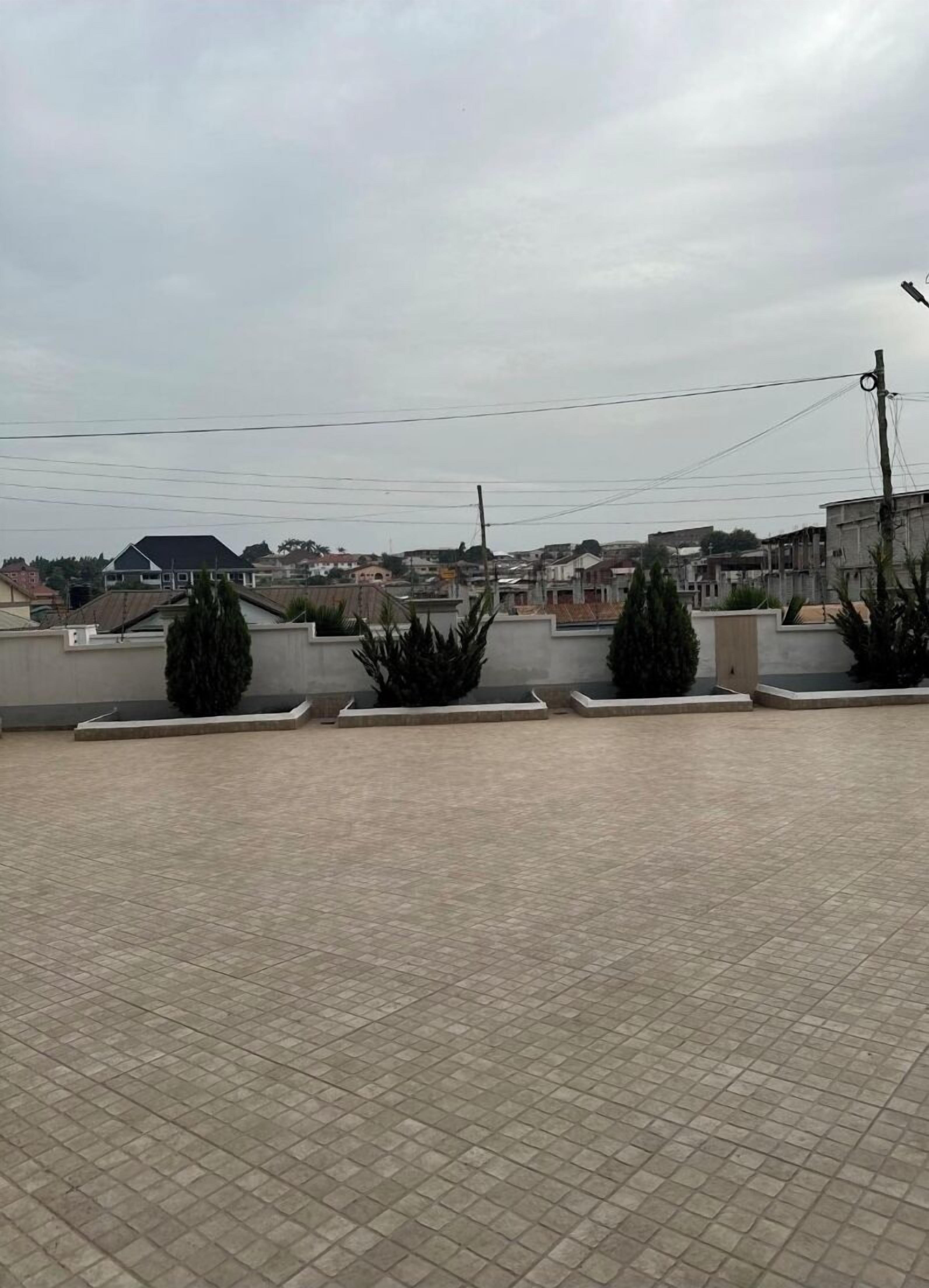 A rooftop terrace with tiled flooring and low walls, surrounded by residential buildings.