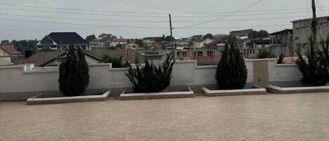 A rooftop terrace with tiled flooring and low walls, surrounded by residential buildings.