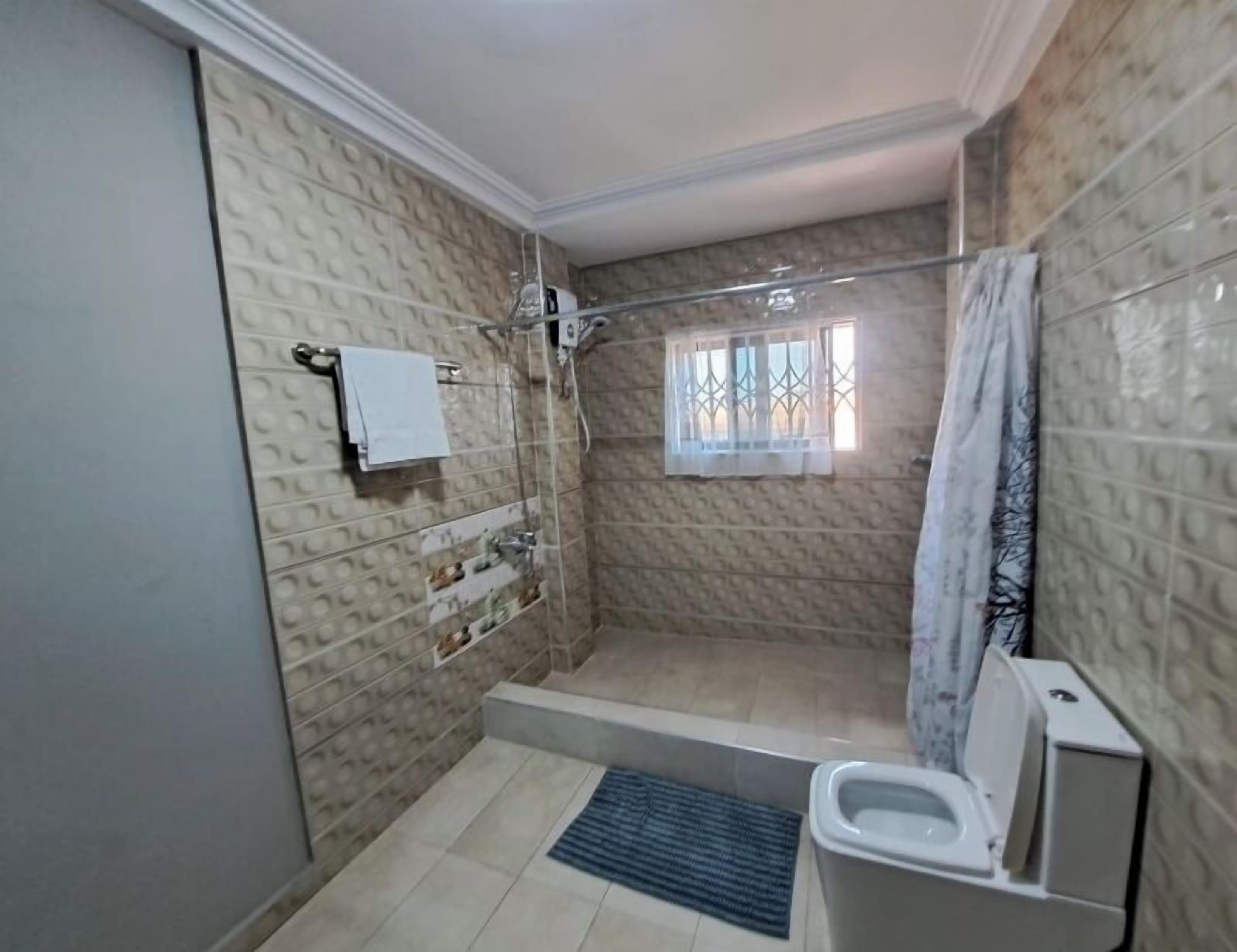 Une salle de bain avec douche, toilettes et une fenêtre avec des barreaux.