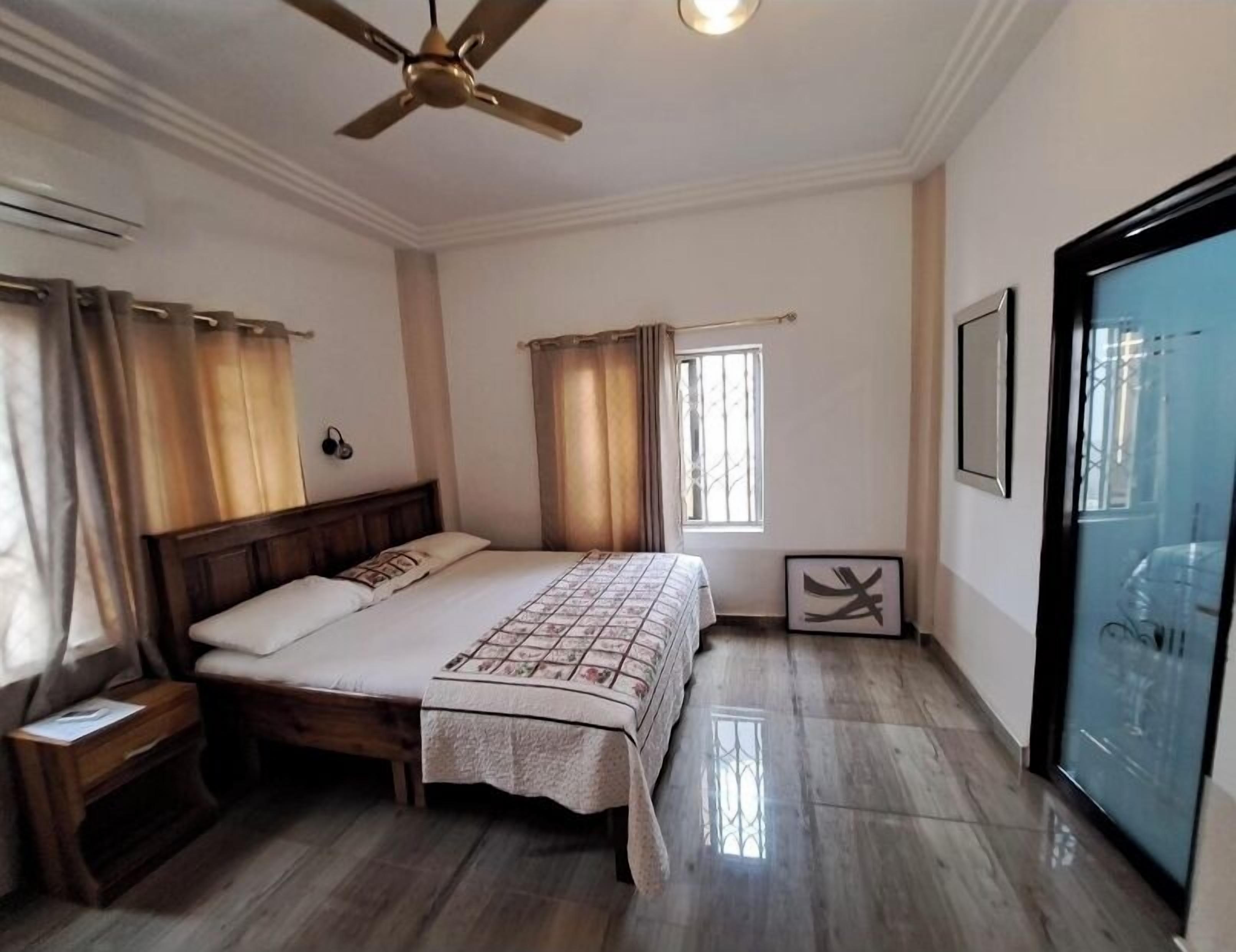 A bedroom with a bed, wooden floor, ceiling fan, and a window with curtains.