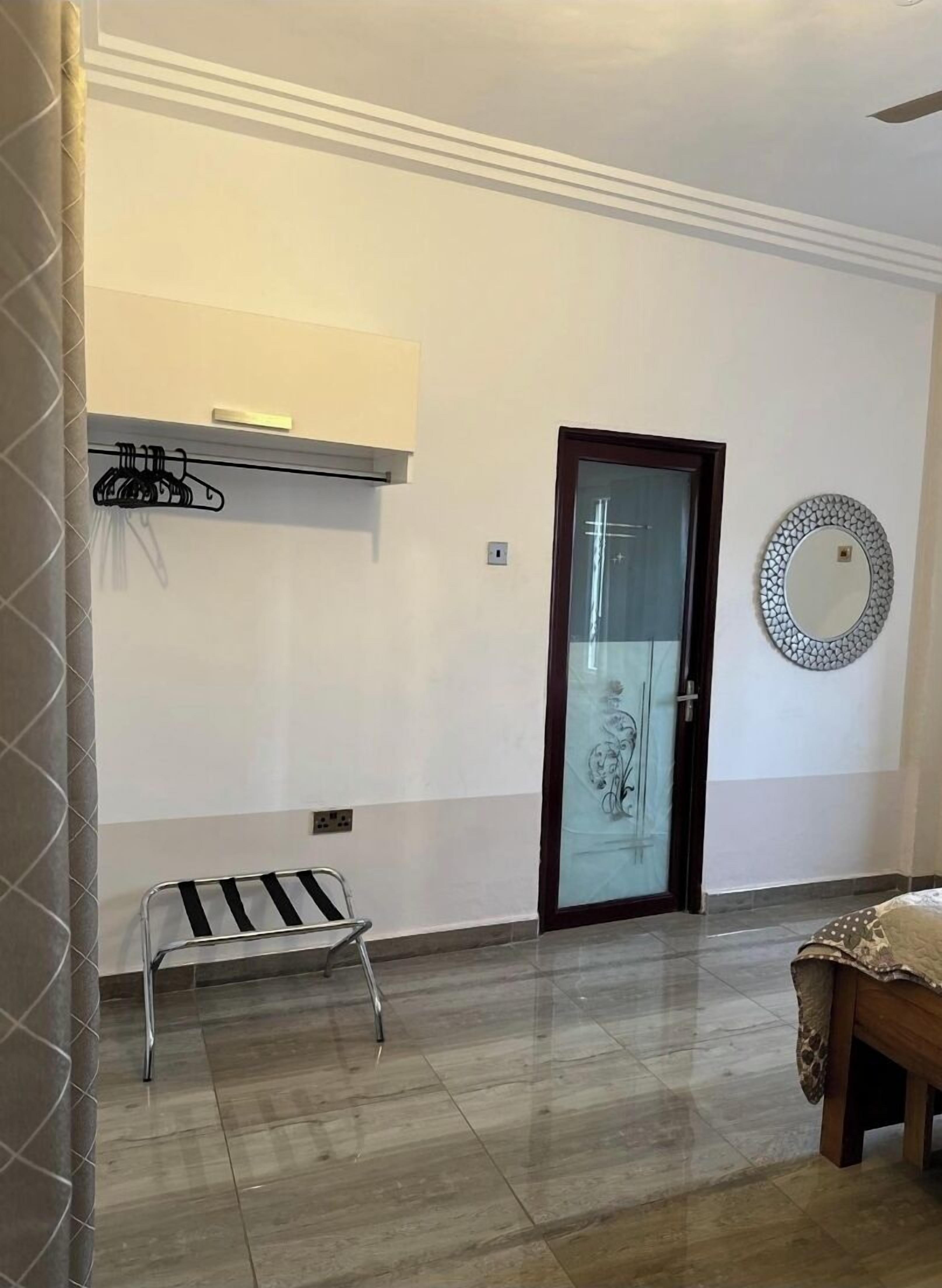 A room with a tiled floor, a bench, a coat rack, a door with a glass panel, and a decorative mirror.