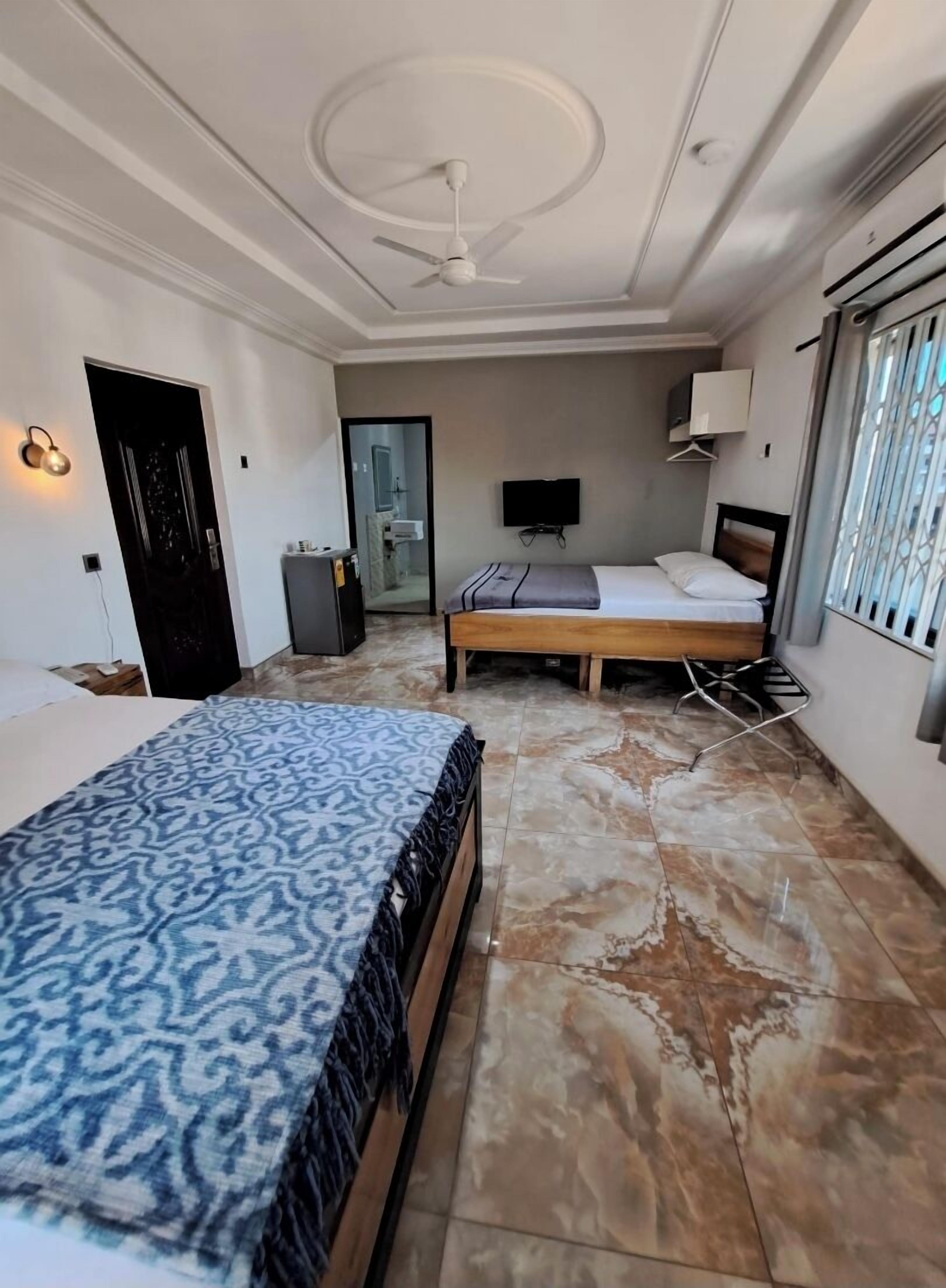 A bedroom with a bed, a ceiling fan, a TV, and a bathroom visible through an open door.