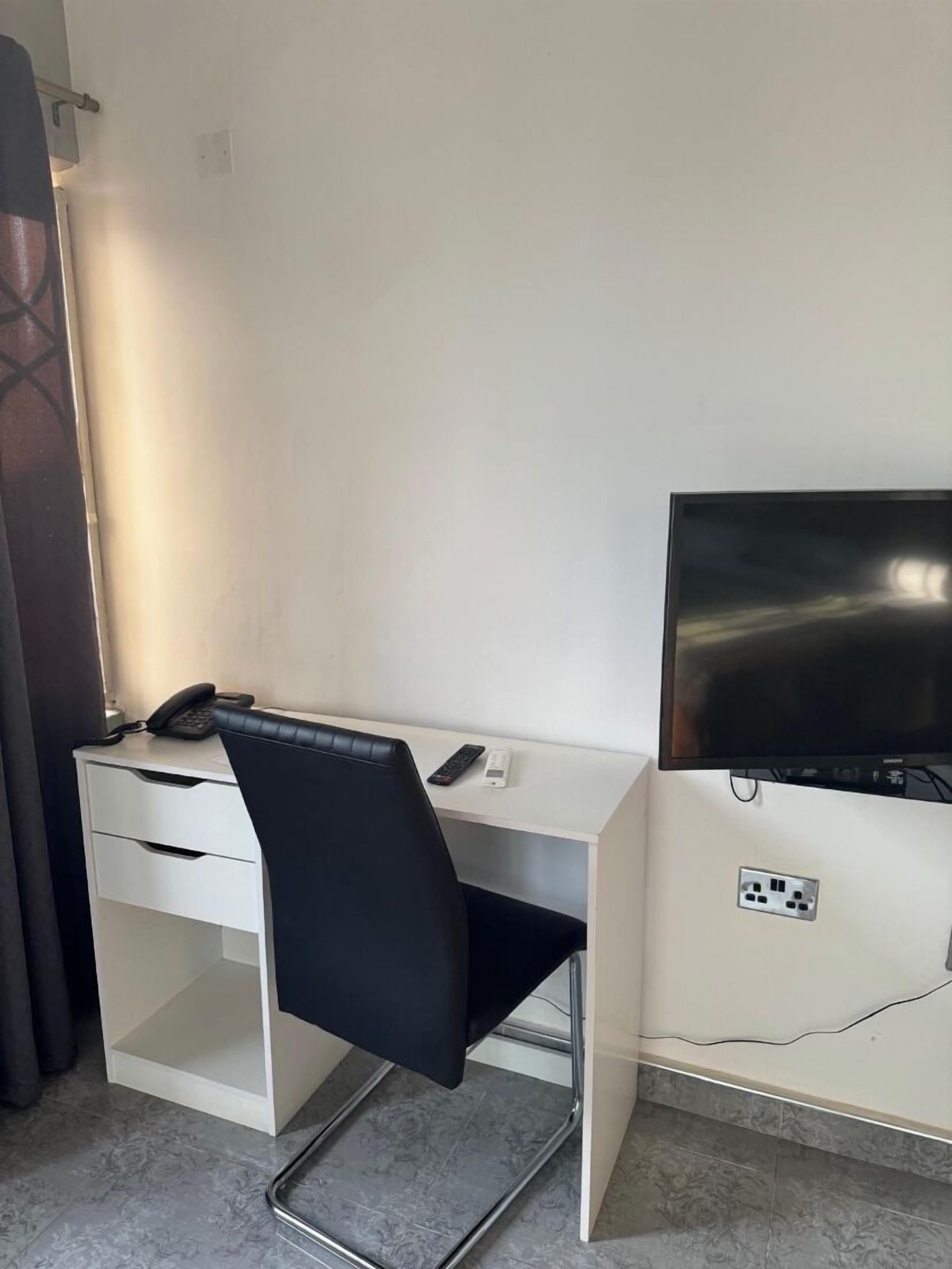 A hotel room with a white desk, a black office chair, a flat-screen TV, and a telephone.