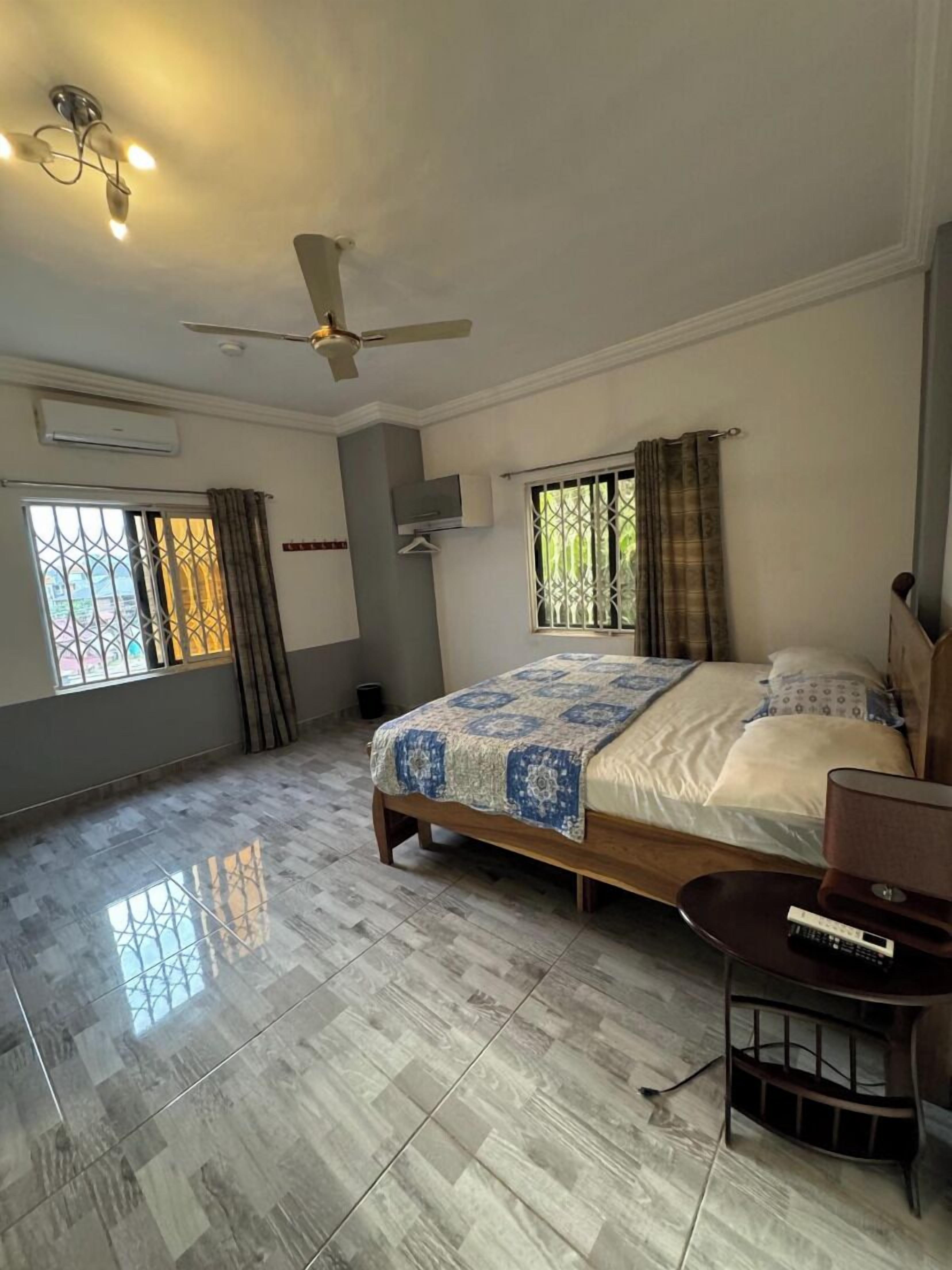 A spacious bedroom with a large bed, a ceiling fan, a small table, and a window with curtains.