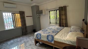 A spacious bedroom with a large bed, a ceiling fan, a small table, and a window with curtains.