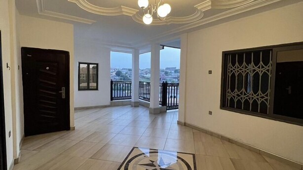 A spacious hallway with a high ceiling, a chandelier, and a view to the outside. - BAFFOUR APARTMENTS (Kumasi)