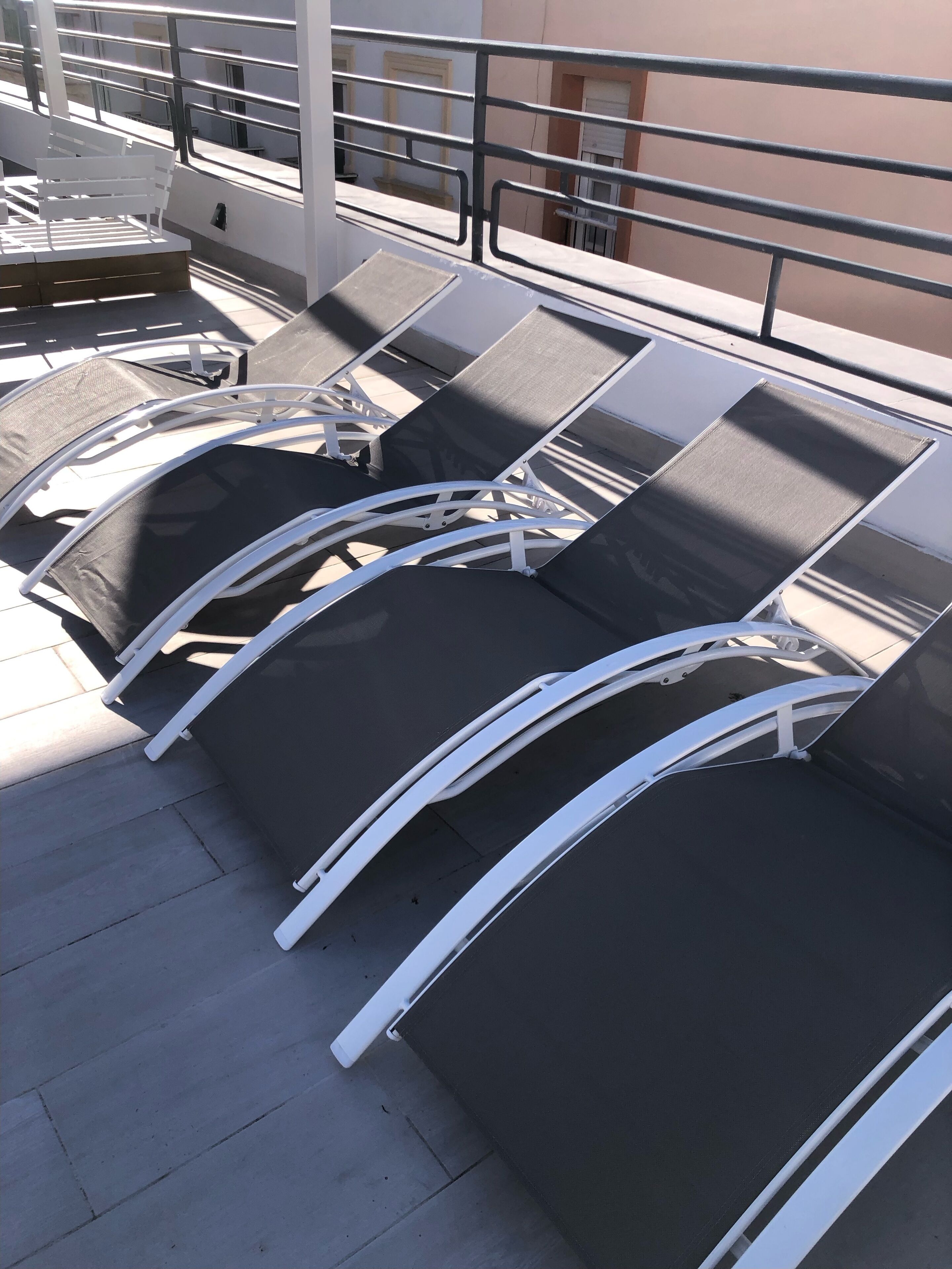 Una hilera de sillones reclinables negros con estructura metálica blanca en una terraza en la azotea.