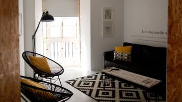 A modern living room with a black and white patterned rug, a black chair with a yellow cushion, a black sofa with a geometric pillow, and a black floor lamp.