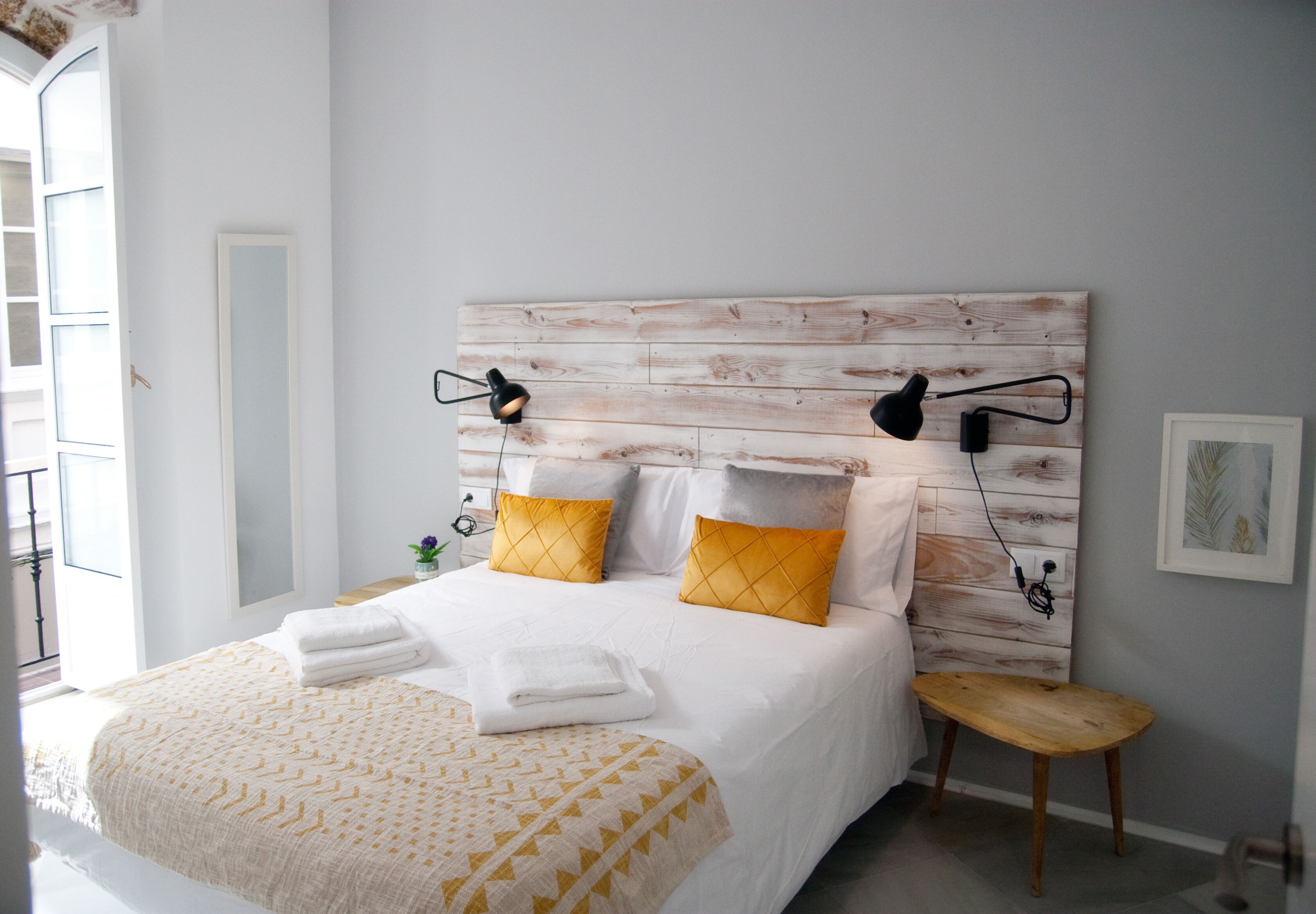 Een opgemaakt bed met witte en gele lakens, een houten hoofdbord en bedlampen.
