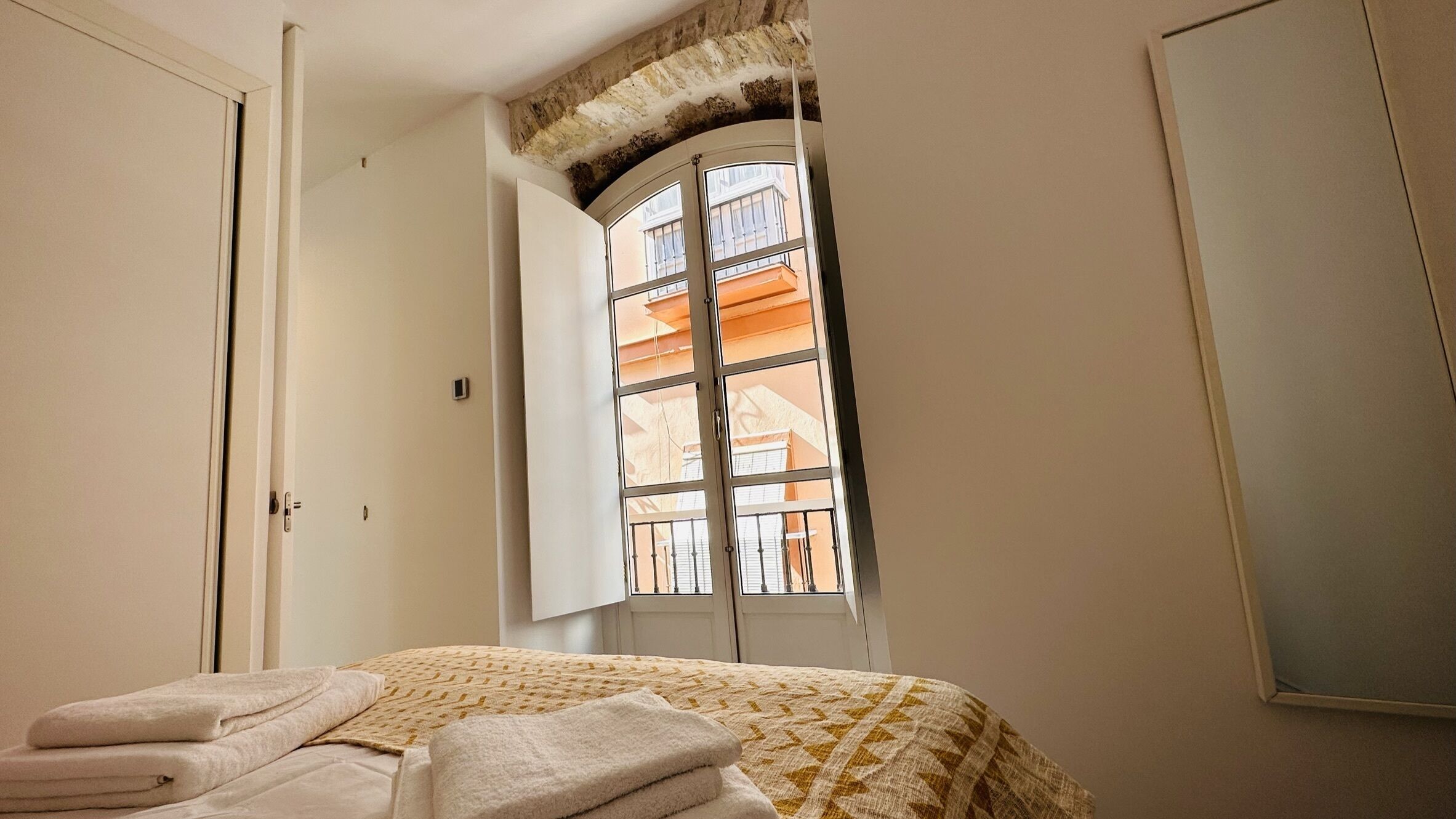 A bedroom with a bed, a window with a view of buildings, and a door.