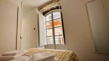A bedroom with a bed, a window with a view of buildings, and a door.