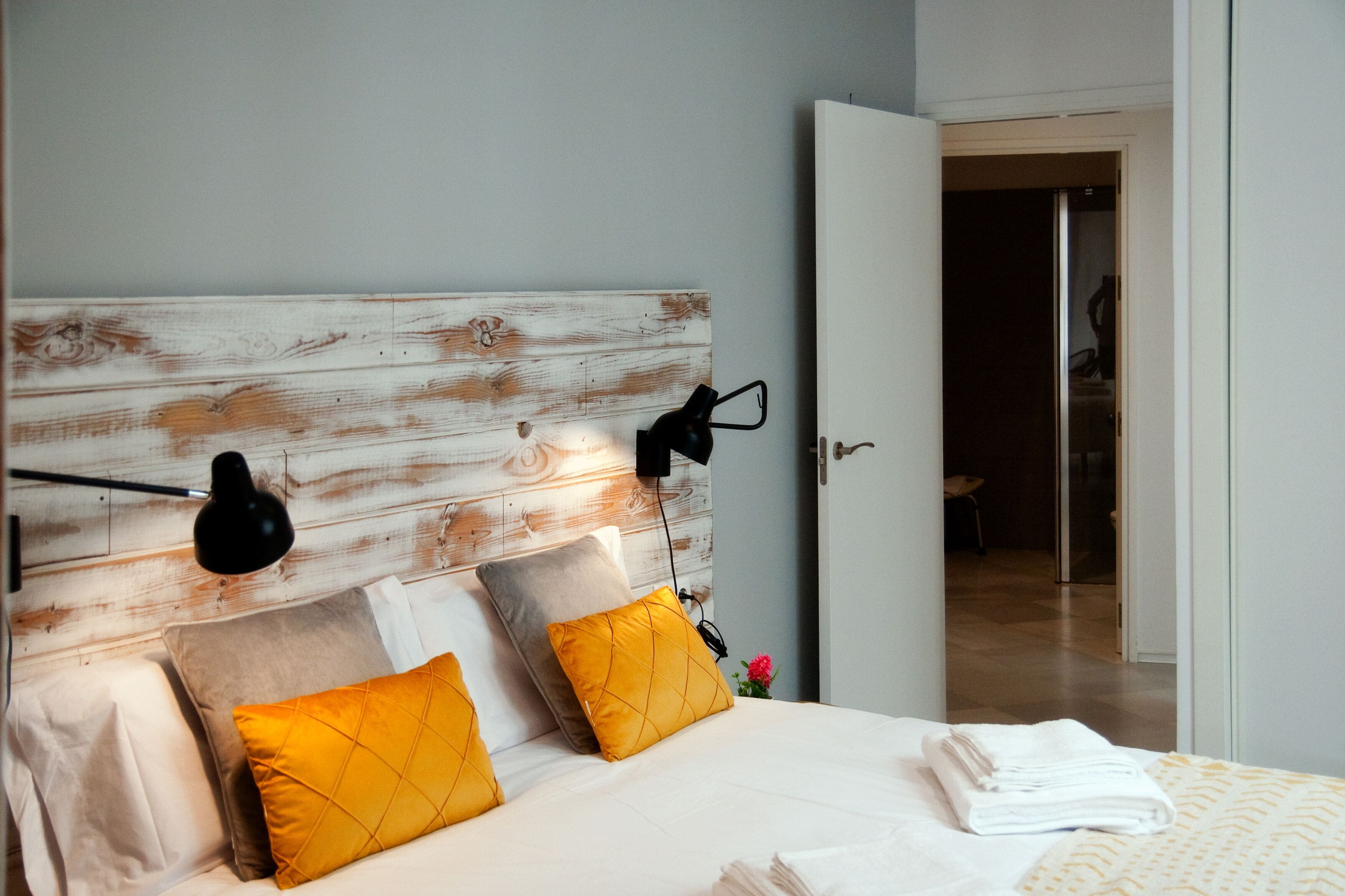 Un dormitorio con cabecera de madera, dos lámparas de noche y una cama bien hecha con almohadas amarillas y blancas.