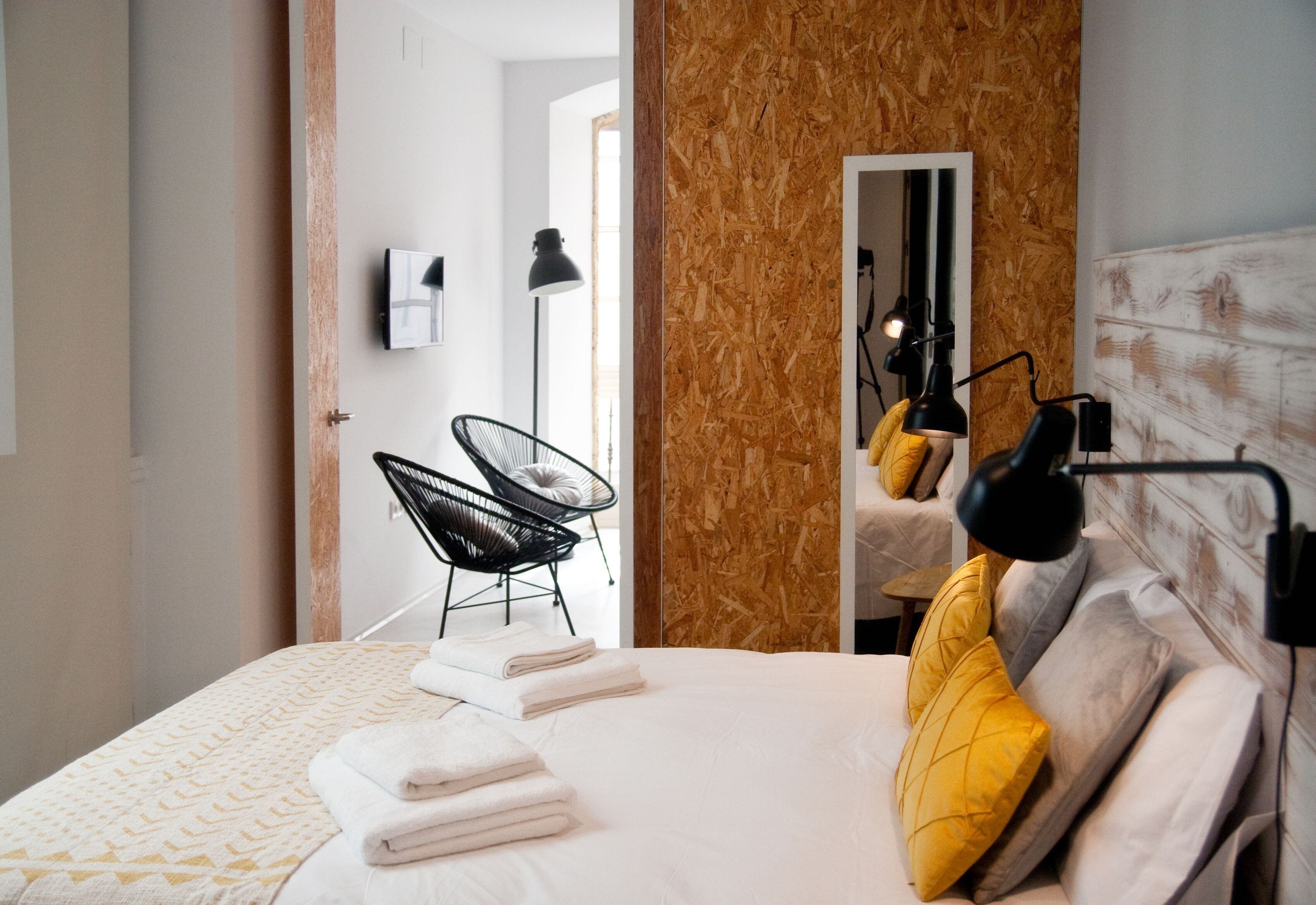 Et moderne hotelværelse med en stor seng, en væg med trædetaljer, en sort stol og en skrivebordslampe.