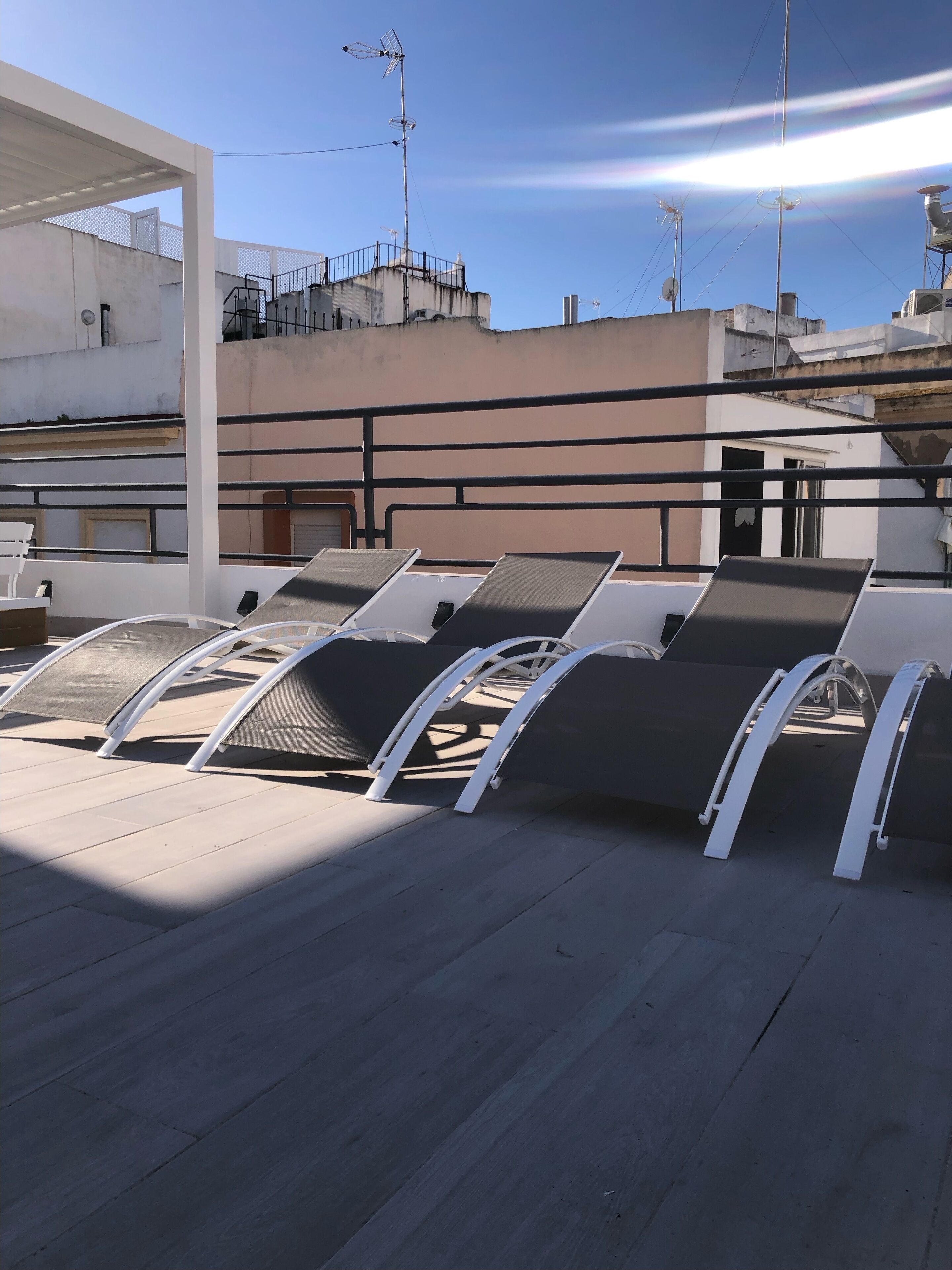 A rooftop terrace with sun loungers and a view of surrounding buildings.