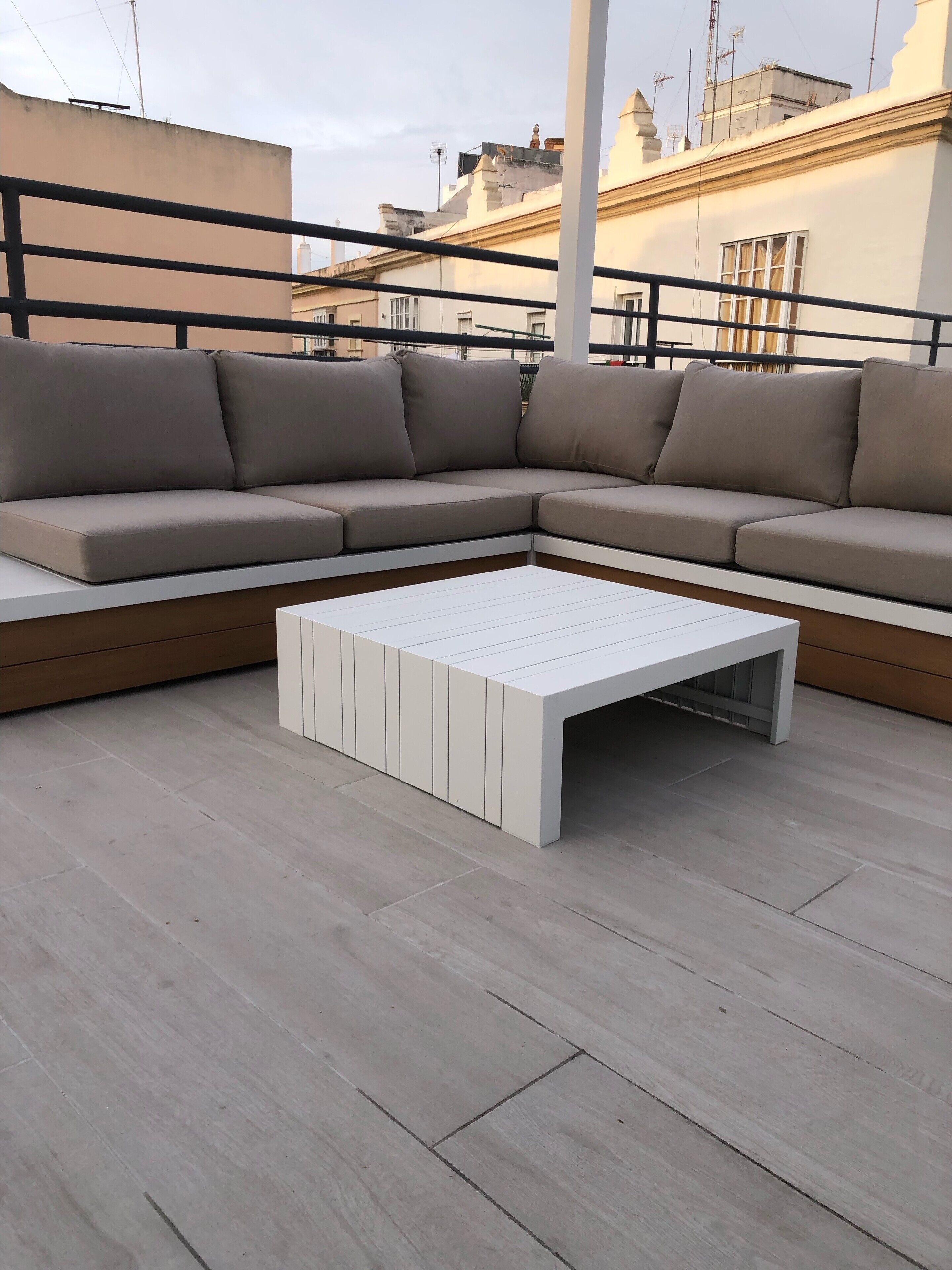 Un área de estar al aire libre moderna con un sofá seccional color beige y una mesa de centro blanca.