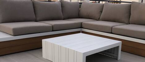 Un área de estar al aire libre moderna con un sofá seccional color beige y una mesa de centro blanca.