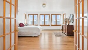 Un dormitorio amplio con una cama grande, suelo de madera y vistas por las ventanas.