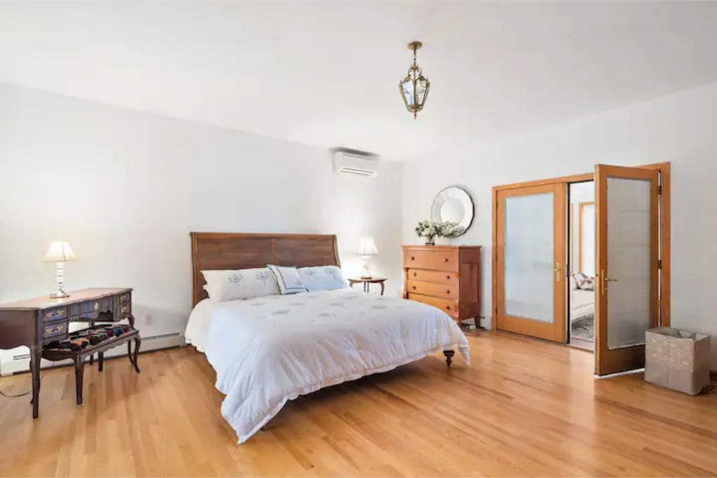 A bedroom with a wooden bed, a dresser, a mirror, and a door with frosted glass panels.