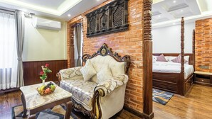 Habitación de hotel con pared de ladrillo decorativa, una cama con dosel, un sofá y una pequeña mesa con frutero.
