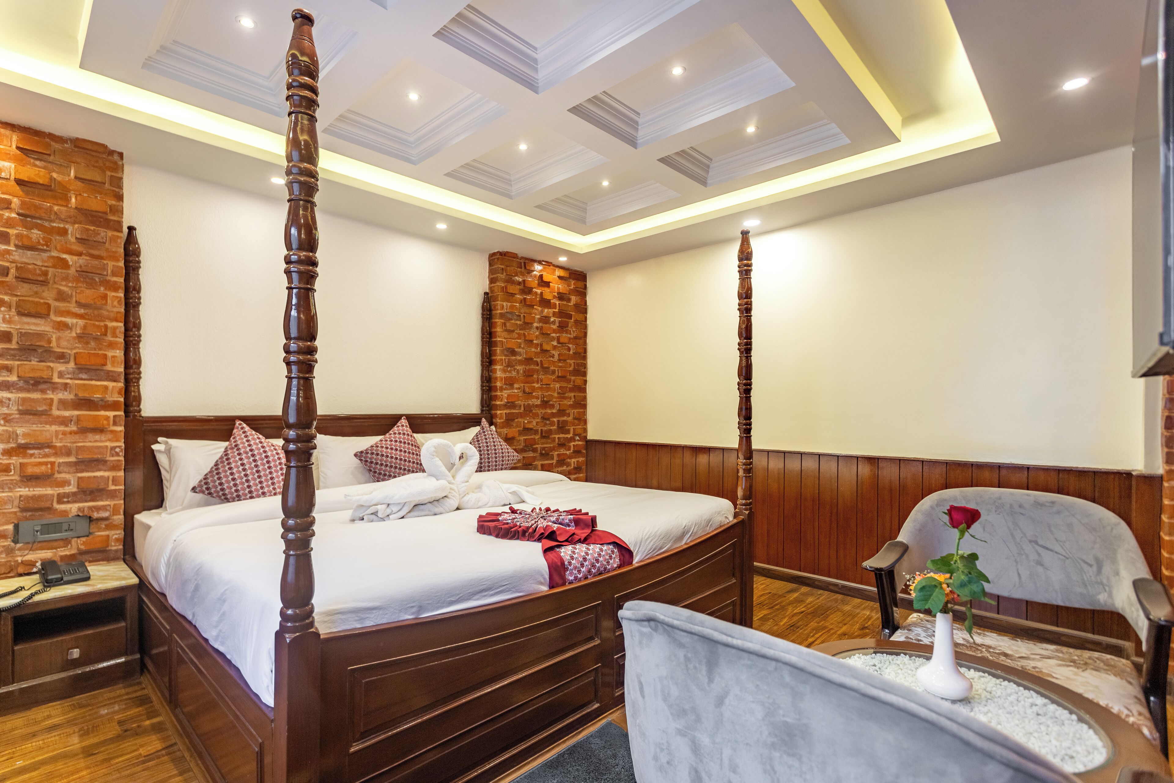 A four-poster bed with a brick accent wall, a wooden headboard, and a bedside table with a telephone.