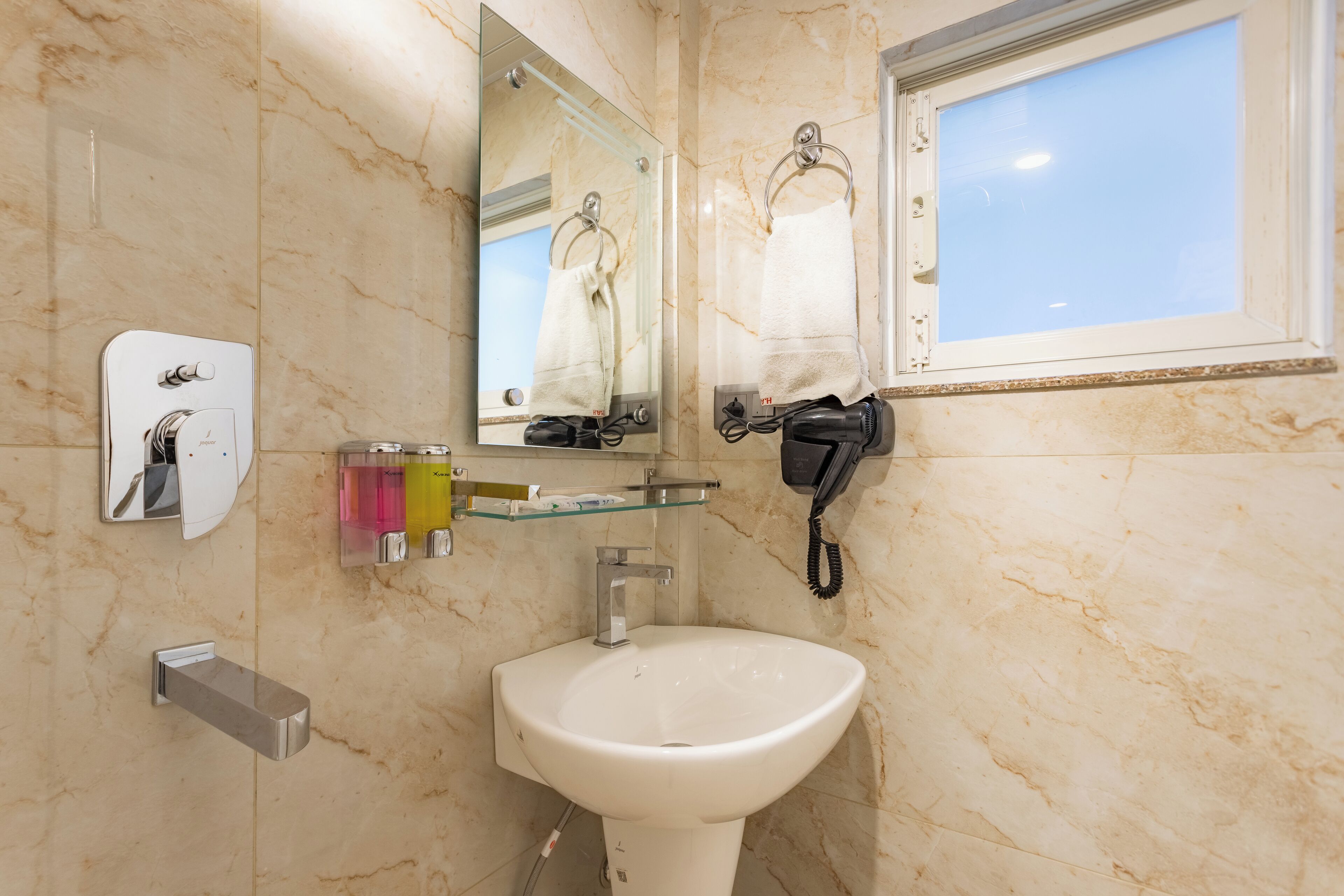 Ein Badezimmer mit Marmorwand, Waschbecken, Spiegel, Handtuchhalter und Fenster.