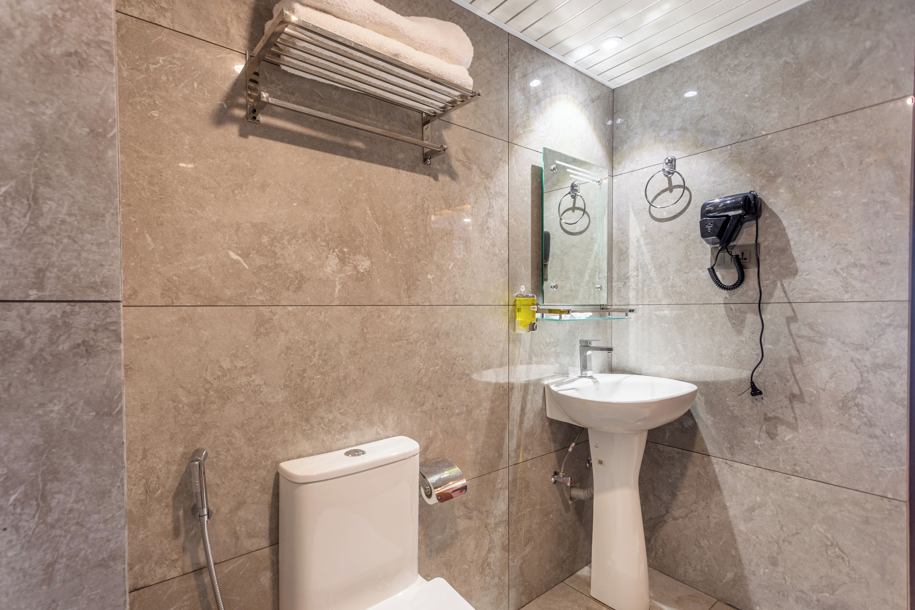 A modern bathroom with a white sink, toilet, and shower. A towel rack and hairdryer are mounted on the wall.