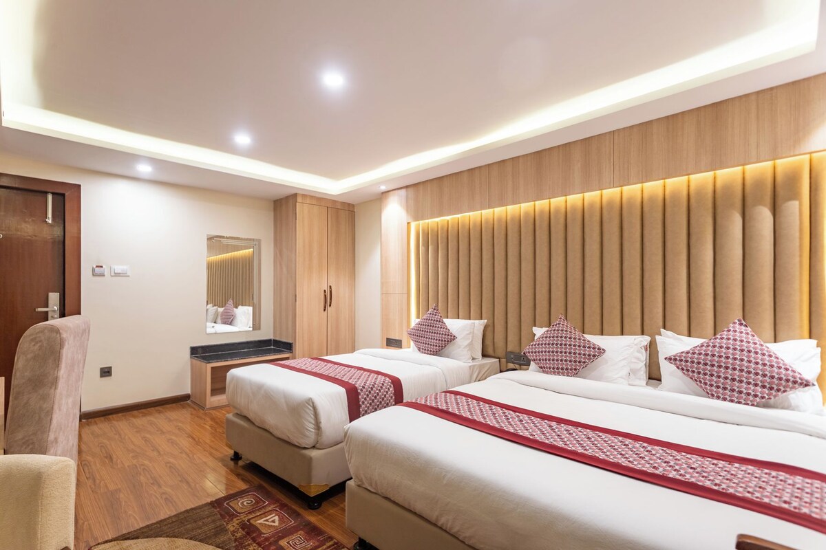 Quarto de hotel com duas camas, cabeceira de madeira, espelho e uma escrivaninha.