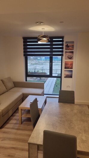 Relax in this serene space with a large window offering a view of the outdoors, a comfortable beige sofa, and a coffee table for your belongings.