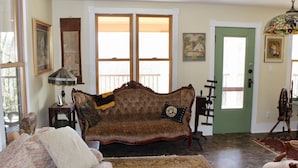 A living room with a vintage sofa, a patterned rug, and a green door. - Charming 1920s Hillside Home Overlooking Valley and Rails-To-Trails (Rimersburg)