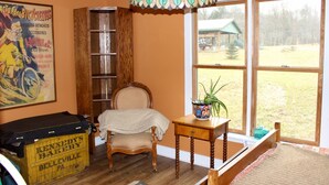 A room with a vintage bicycle poster, a wooden ladder, a chair, a table with a plant, and a large window with a view of the outdoors. - Charming 1920s Hillside Home Overlooking Valley and Rails-To-Trails (Rimersburg)